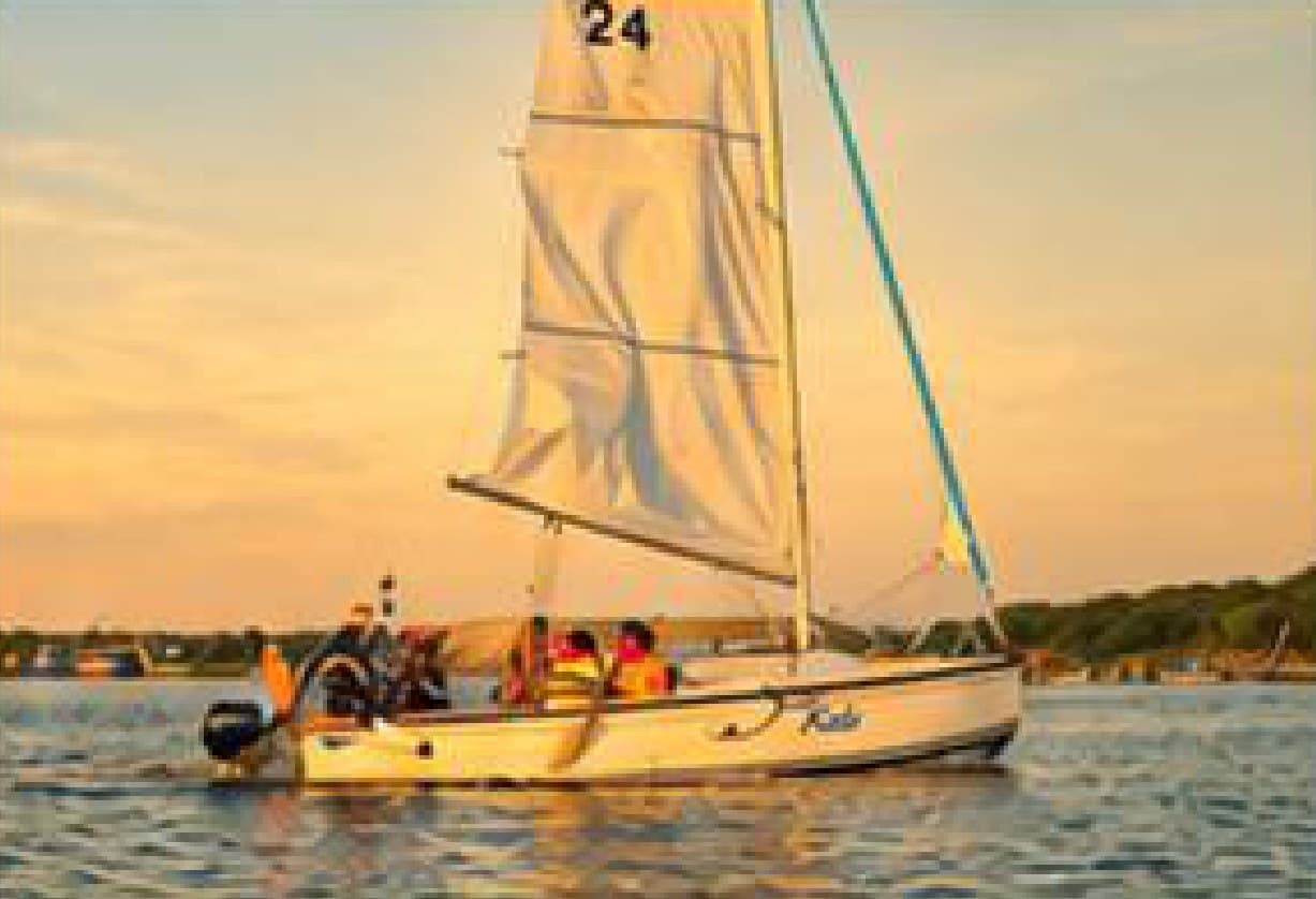 A small sailboat with its sail raised, out on the backwaters at sunset.