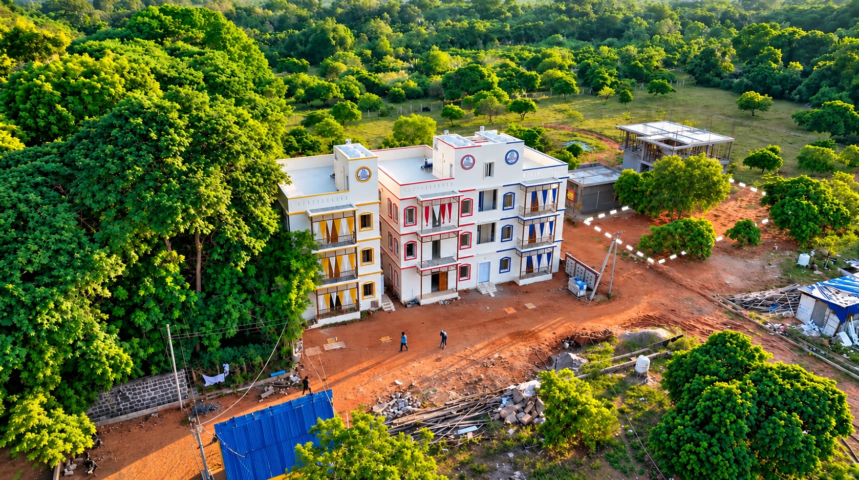 Low aerial view of the outlined villa plot beside a completed Auroma building, with dense greenery beyond.